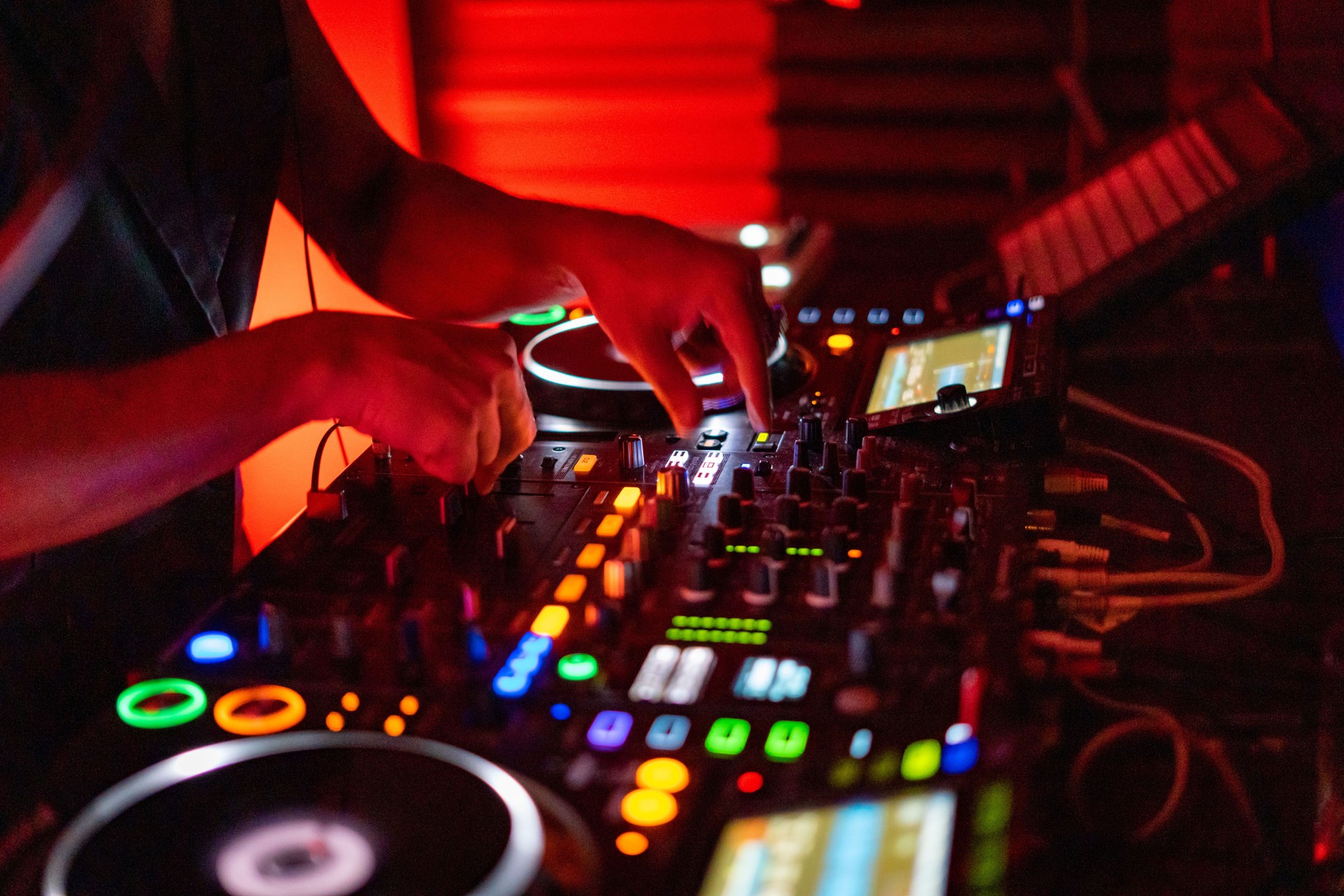 DJ working on a professional controller in a dimly lit room, with illuminated buttons