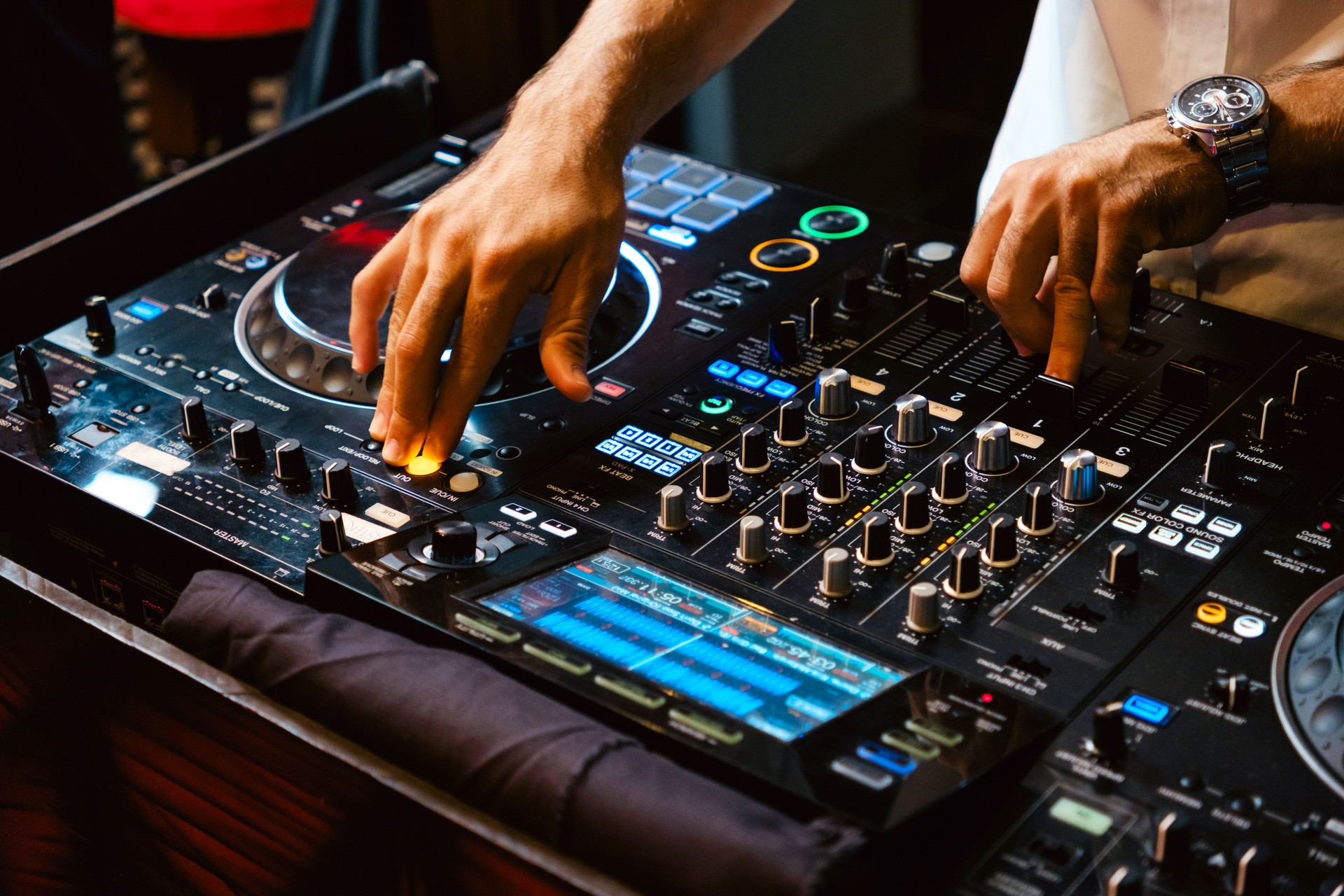 A DJ skillfully manipulates a mixing console, blending tracks to create an electrifying atmosphere at a lively event.